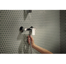 Eine Hand hält einen Duschschlauch an einer Hansgrohe Einhebel Duscharmatur vor einer Wand mit sechseckigen Mosaikfliesen.