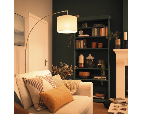 Moderne Bogenlampe mit Stoffschirm neben einem Sofa in einem gemütlich eingerichteten Wohnzimmer mit dunklem Regal und Kamin.