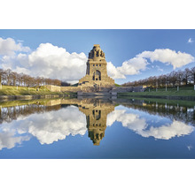 Das Völkerschlachtdenkmal in Leipzig spiegelt sich bei Sonnenschein im Wasserbecken vor dem monumentalen Bauwerk aus Naturstein wider.