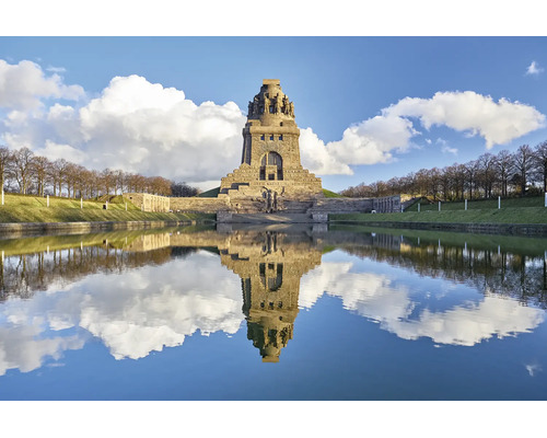 Das Völkerschlachtdenkmal in Leipzig spiegelt sich bei Sonnenschein im Wasserbecken vor dem monumentalen Bauwerk aus Naturstein wider.