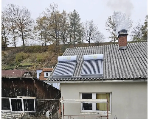 Zwei Röhrenkollektoren für die Solaranlage auf einem geneigten Dach eines Wohnhauses mit Kamin.