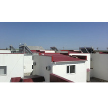 Solarthermieanlagen auf den roten Dächern moderner weißer Gebäude bei klarem Himmel.