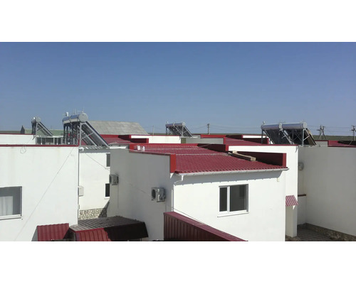 Solarthermieanlagen auf den roten Dächern moderner weißer Gebäude bei klarem Himmel.