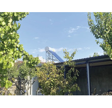 Solarthermieanlage mit Solarspeicher auf einem Flachdach im Garten mit Bäumen im Vordergrund.