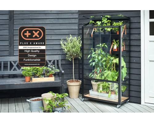Ein mobiles Gewächshaus mit Glasfront und Holzregalen auf einer Terrasse, ausgezeichnet mit dem Plus X Award für hohe Qualität und Funktionalität.