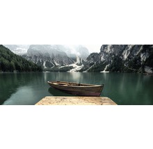 Ein Holzboot liegt an einem Steg an einem See mit Bergkulisse.