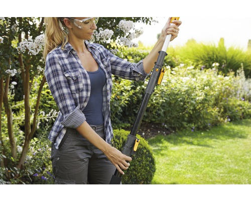 Eine Frau mit Schutzbrille bedient eine hochentaster im Garten.