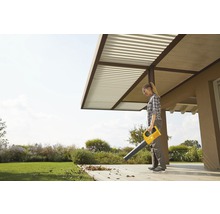 Eine Frau benutzt einen gelben Laubbläser im Garten, um Blätter zu entfernen.