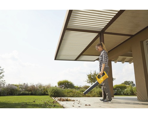 Eine Frau benutzt einen gelben Laubbläser im Garten, um Blätter zu entfernen.