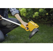 Eine Person bedient einen gelben Rasentrimmer im Garten.