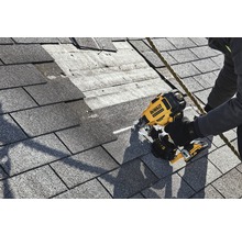 Ein Arbeiter befestigt Dachschindeln mit einem Druckluftnagler von DeWalt auf einem Dach.
