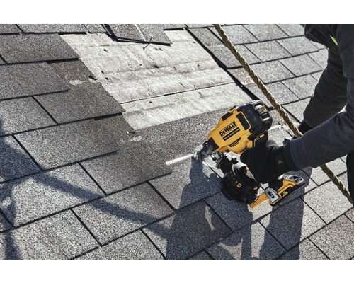 Ein Arbeiter befestigt Dachschindeln mit einem Druckluftnagler von DeWalt auf einem Dach.