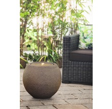 Dekorativer Kugelbrunnen aus Stein neben Korbsessel im Garten
