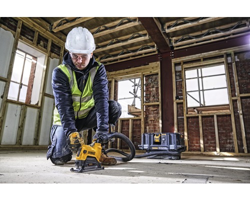 Ein Bauarbeiter in Schutzkleidung bedient eine Mauernutfräse von DeWalt auf einer Baustelle.