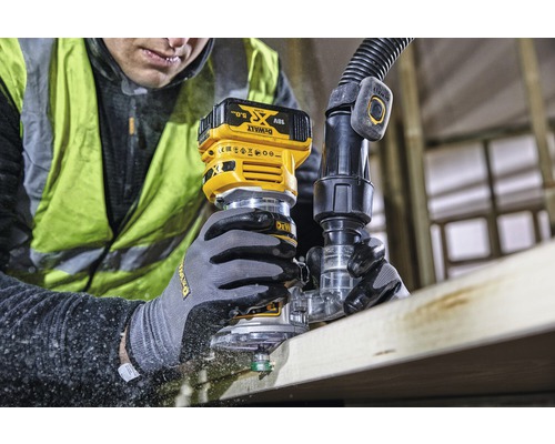 Mann fräst mit einer Akku Oberfräse ein Holzbrett. Angeschlossen ist ein Absaugschlauch. Marke: DeWalt