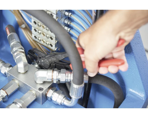 Hand, die mit einer Zange an einer Hydraulikleitung arbeitet
