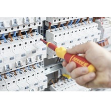 Ein Elektriker arbeitet mit einem isolierten Schraubendreher an einer elektrischen Anlage.