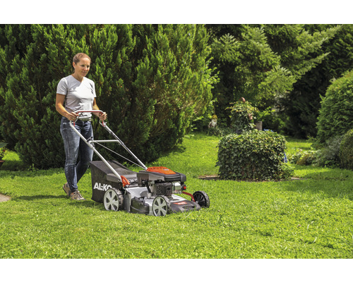 Frau bedient Rasenmäher im Garten.