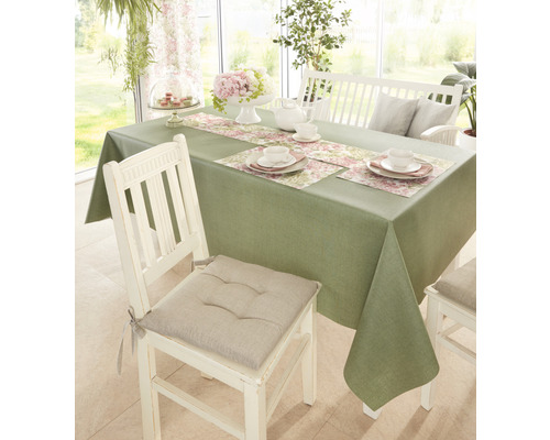 Gedeckter Esstisch mit grüner Tischdecke, Tischläufer mit Blumenmuster und weißem Geschirr.