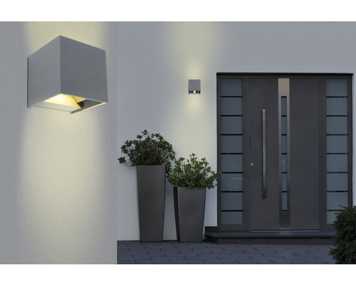 Szene mit Hauswand, zwei Außenleuchten und einer Haustür mit Pflanzenkübeln