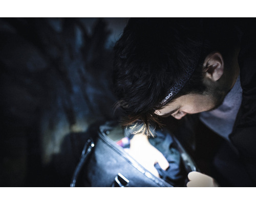 Mann mit Stirnlampe durchsucht eine Tasche im Dunkeln.