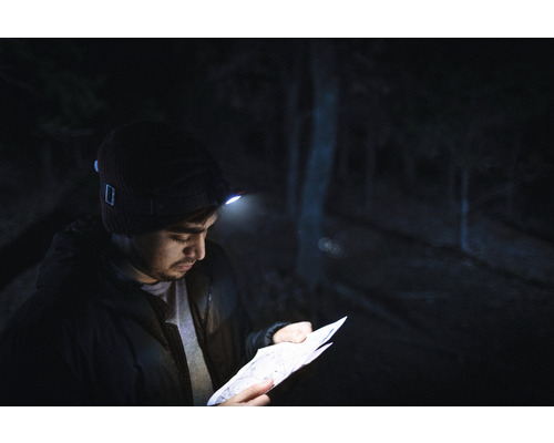 Mann mit Stirnlampe liest eine Karte im Dunkeln.