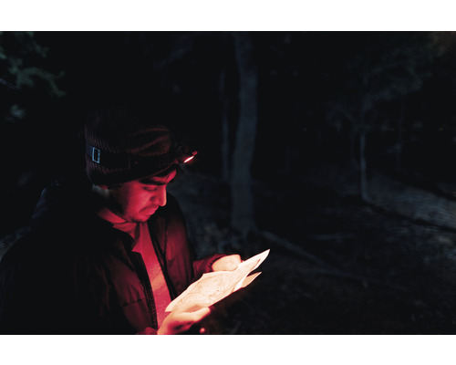Mann mit Stirnlampe liest eine Karte im Dunkeln.
