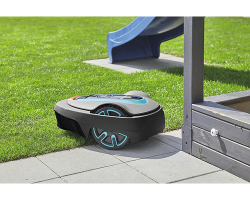 Rasenmähroboter auf Rasen neben einer Rutsche und einem Sandkasten