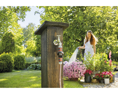 Frau gießt Blumen mit einem Gartenschlauch an einem Wasserhahn im Garten