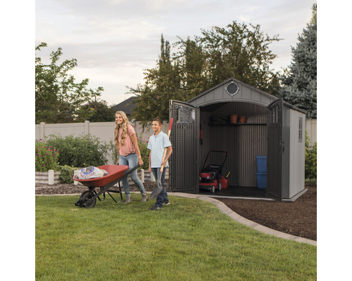 Gartenszene mit einem Geräteschuppen, einer Schubkarre und zwei Personen, die Gartenarbeiten verrichten