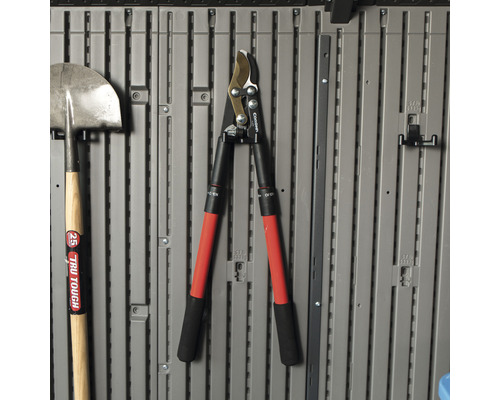 Gartengeräte wie Spaten und Heckenschere hängen an einer grauen Wand