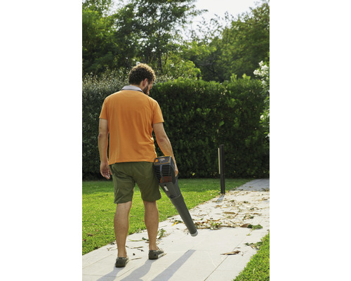 Eine Person benutzt einen Laubbläser, um Blätter von einem Gehweg zu entfernen.