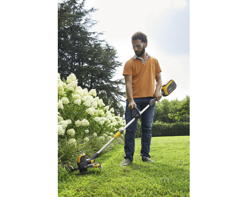 Ein Mann benutzt einen Akku-Rasentrimmer im Garten, um Gras zu schneiden.