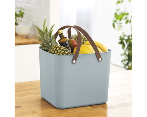 Blauer Korb mit Griffen, gefüllt mit Obst auf einem Holztisch.