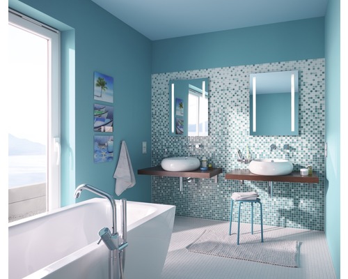 Helles Badezimmer mit Badewanne, zwei Waschbecken, beleuchteten Spiegeln und mosaikgefliesten Wänden