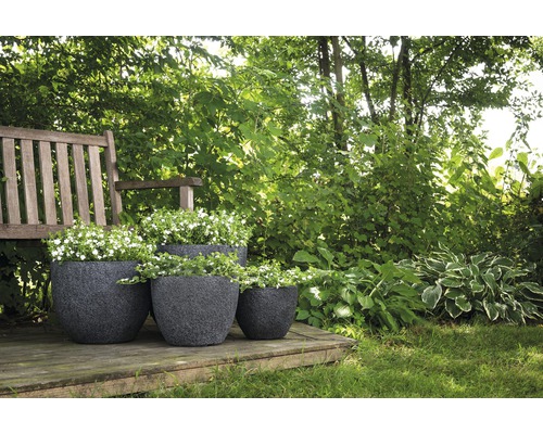 Drei bepflanzte, dunkle Pflanzgefäße aus Kunststoff auf einer Holzterrasse in einem Garten.