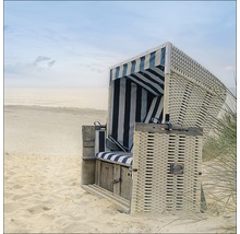 Strandkorb aus Korbgeflecht mit gestreiften Polstern am Strand