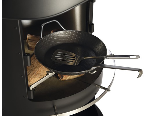 Detailansicht eines Grillgeräts mit Holz, Bratpfanne und Pfannenwender