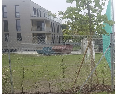 Außenansicht eines Mehrfamilienhauses mit Rasenfläche und Zaun.