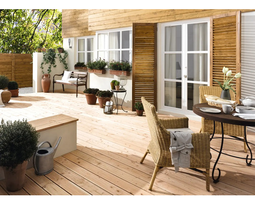Helle Holzterrasse mit Gartenmöbeln, Pflanzen und dekorativen Elementen vor einem Haus mit Holzfassade