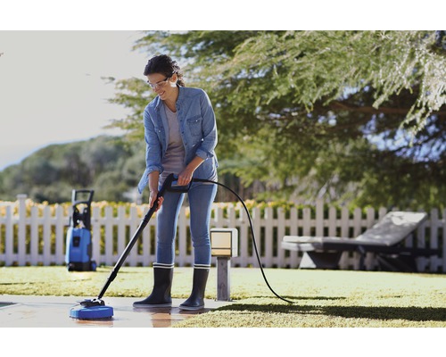 Frau reinigt Terrasse mit Hochdruckreiniger im Garten