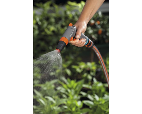 Eine Hand hält eine Gartenspritze, aus der Wasser strömt, zur Bewässerung von Pflanzen.