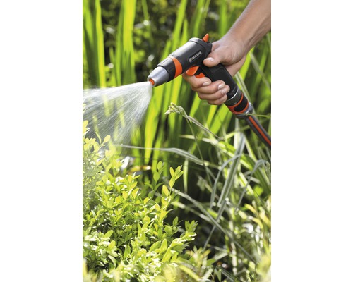 Eine Hand hält eine Gartenspritze, die Wasser auf Pflanzen sprüht.