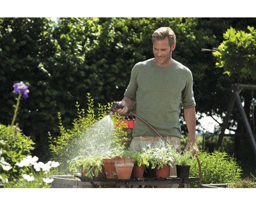 Ein Mann bewässert Pflanzen im Garten mit einer Gartenspritze und einem Gartenschlauch.