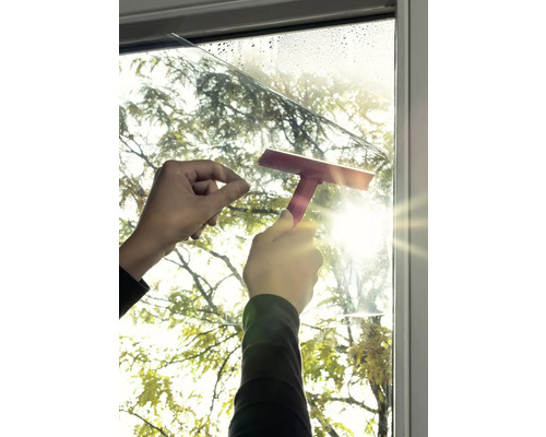 Außenaufnahme von einer Person, die eine Fensterfolie mit einem Rakel anbringt