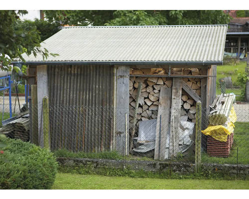 Holzschuppen mit Brennholz und Wellblechdach hinter Maschendrahtzaun