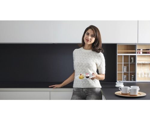 Moderne Küche mit weißen Schränken und dunkler Arbeitsplatte, Frau mit Teller und Gebäck