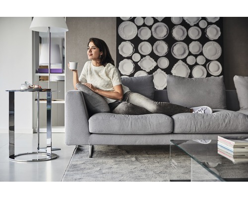 Frau entspannt auf einem grauen Sofa in einem Wohnzimmer mit modernem Dekor.