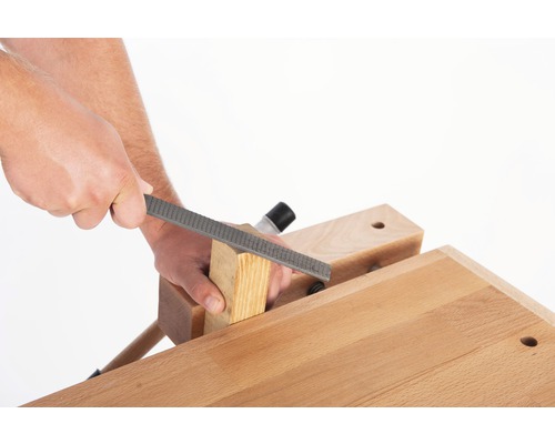 Handwerker bearbeitet Holzstück mit einer Holzraspel auf einer Werkbank