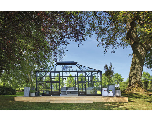 Gewächshaus mit Stahlrahmen und Glas auf Holzterrasse in Gartenumgebung
